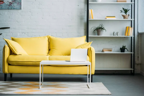 Laptop on table near yellow sofa in living room — Stock Photo