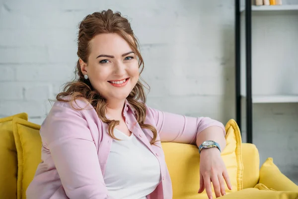 Porträt einer schönen lächelnden Frau, die auf dem Sofa sitzt und zu Hause in die Kamera schaut — Stockfoto