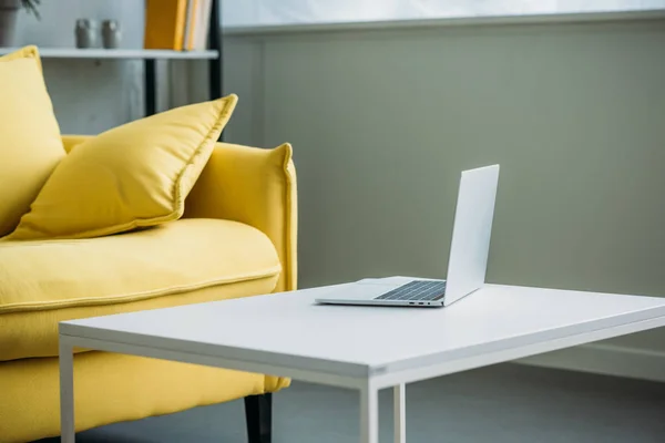 Ноутбук на столі біля жовтого дивана у вітальні — стокове фото