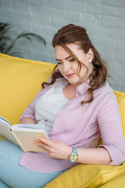 Mulher atraente livro de leitura no sofá em casa — Fotografia de Stock