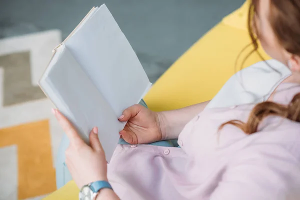 Immagine ritagliata della donna che legge il libro sul divano a casa — Foto stock