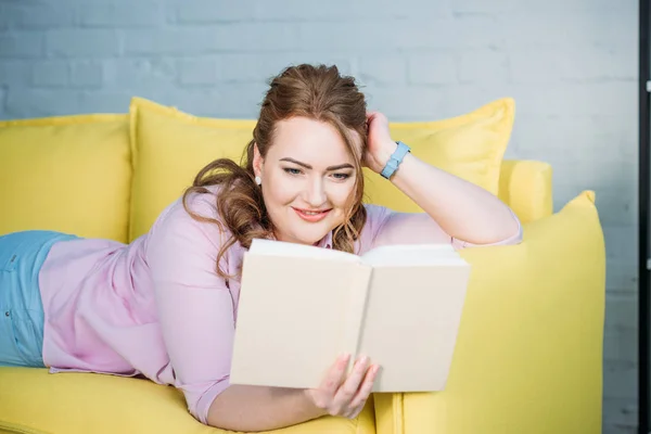 Schöne Frau, die zu Hause auf dem Sofa liegt und Buch liest — Stockfoto