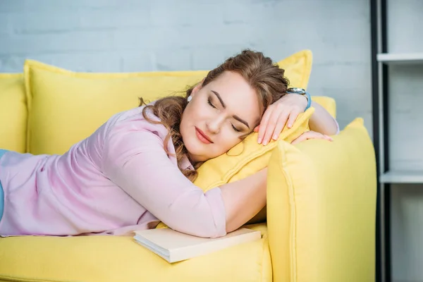Bella donna che dorme sul divano con libro a casa — Foto stock