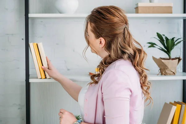 Schöne Frau wählt Buch aus dem Regal zu Hause — Stockfoto