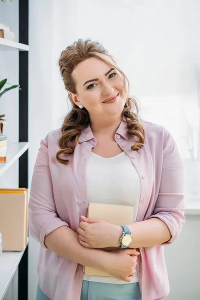 Attraktive Frau hält Buch in der Hand und blickt zu Hause in die Kamera — Stockfoto