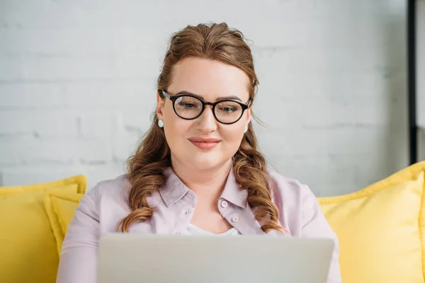 Hermosa freelancer sentado con el ordenador portátil en el sofá en casa - foto de stock