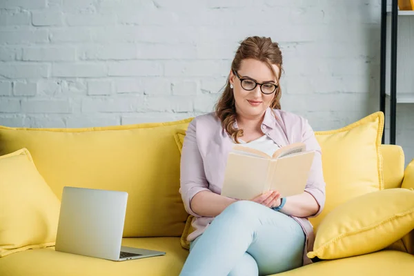 Beautiful woman reading book and studying on sofa at home — Stock Photo