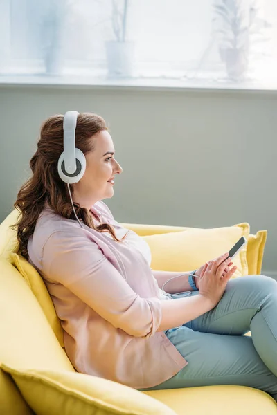 Vista laterale di bella donna che ascolta musica sul divano a casa — Foto stock