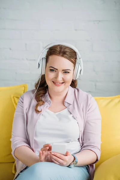 Красивая женщина слушает музыку со смартфоном на диване дома — стоковое фото