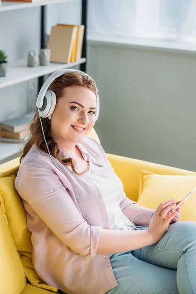 Bela mulher ouvindo música no sofá e olhando para a câmera em casa — Fotografia de Stock