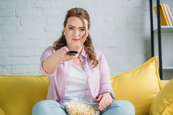 Beautiful woman changing tv channels with remote control at home — Stock Photo
