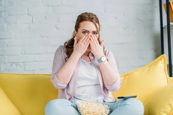 Shocked beautiful woman watching movie with popcorn at home — Stock Photo
