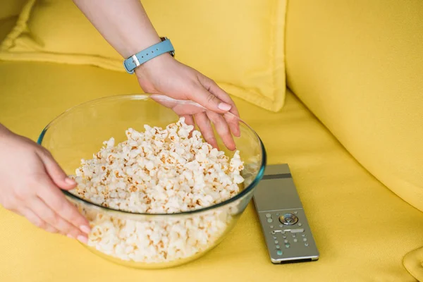 Cropped image of woman putting bowl with popcorn on sofa at home — Stock Photo