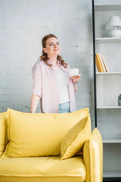 Bella donna in possesso di una tazza di caffè e guardando lontano a casa — Foto stock