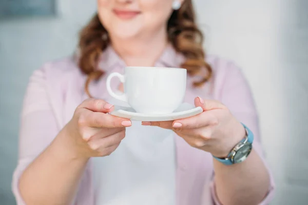 Imagem cortada de mulher mostrando xícara de café em casa — Fotografia de Stock