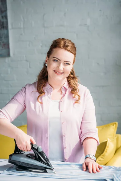 Smiling beautiful woman ironing shirt with iron at home — Stock Photo