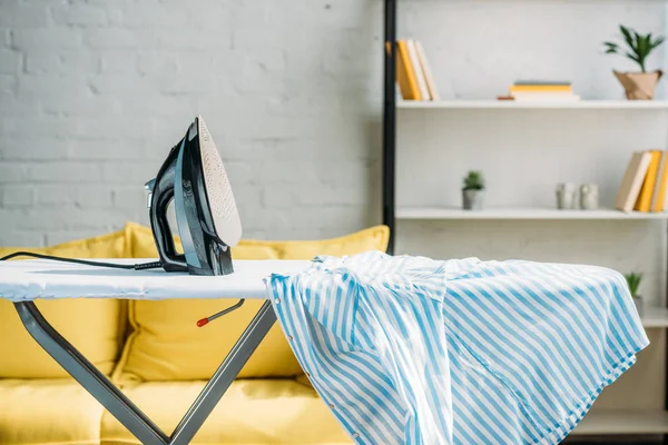 Striped blue shirt and iron on ironing board at home — Stock Photo