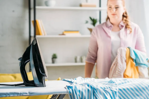 Plancha y camisa en tabla de planchar con hermosa mujer en el fondo en casa - foto de stock