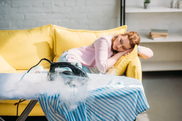 Iron burning on shirt while woman sleeping on sofa at home — Stock Photo