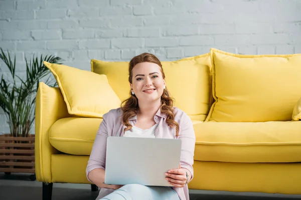 Smiling beautiful woman holding laptop and looking at camera at home — Stock Photo