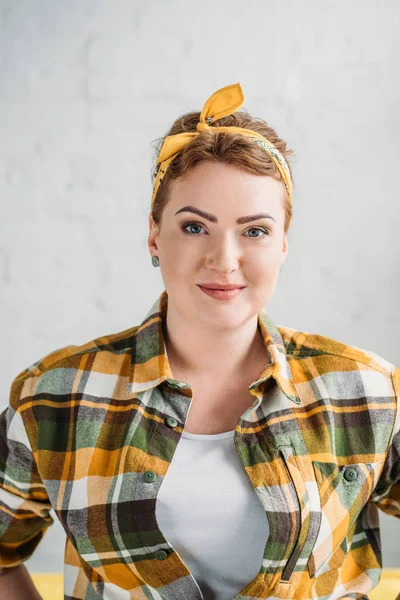Portrait of beautiful woman in checkered shirt and headband looking at camera at home — Stock Photo