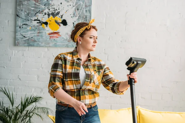 Beautiful woman looking at vacuum cleaner at home — Stock Photo