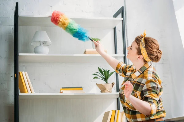 Bella donna spolverare scaffali a casa — Foto stock