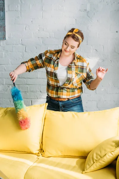 Bela mulher polvilhar sofá amarelo em casa — Fotografia de Stock