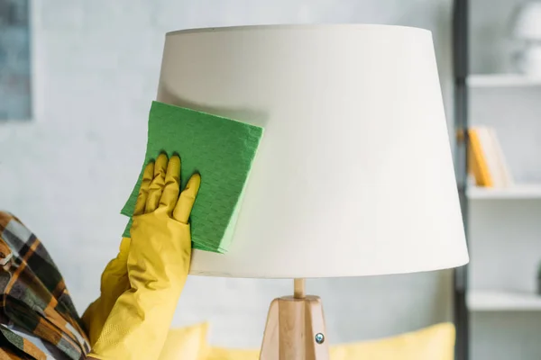 Abgeschnittenes Bild einer Frau, die zu Hause eine Lampe mit Lappen abstaubt — Stockfoto