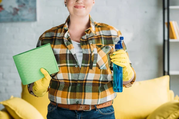 Imagen recortada de la mujer sosteniendo trapo y botella de spray para limpiar en casa - foto de stock