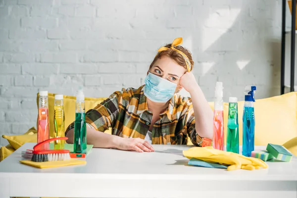 Schöne müde Frau sitzt am Tisch mit Putzmitteln zu Hause — Stockfoto