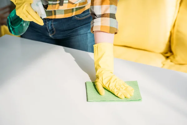 Cropped image of woman cleaning table with spray bottle and rag at home — Stock Photo