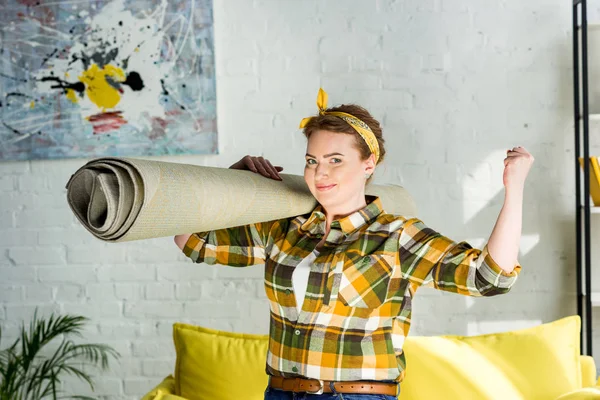 Schöne Frau hält Teppich auf der Schulter und zeigt Muskeln zu Hause — Stockfoto