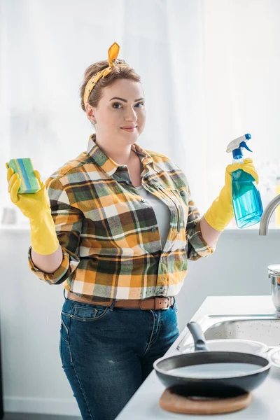 Beautiful woman holding washing sponge and spray bottle while cleaning at kitchen — Stock Photo