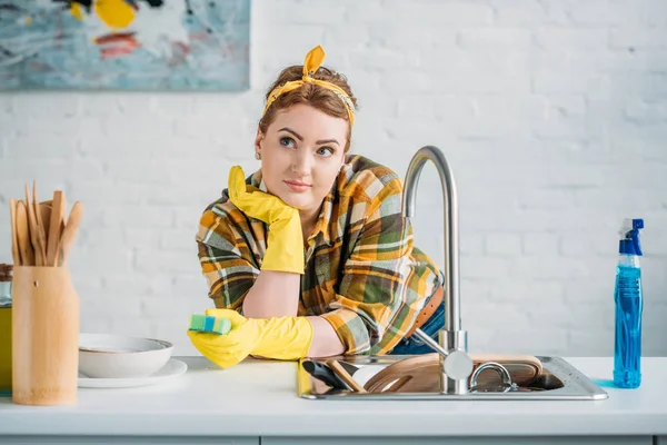 Hermosa mujer apoyada en el mostrador de la cocina y la celebración de esponja de lavado - foto de stock