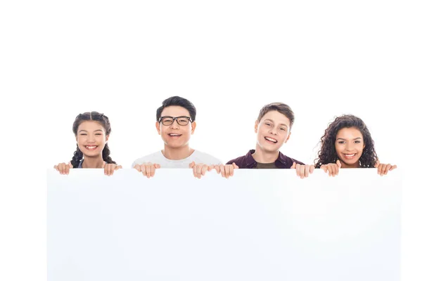 Retrato de adolescentes multirraciais sorridentes segurando banner em branco isolado no branco — Fotografia de Stock