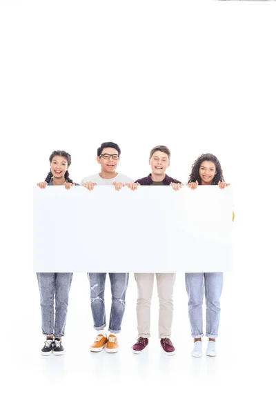 Smiling multiracial teenagers holding blank banner together isolated on white — Stock Photo