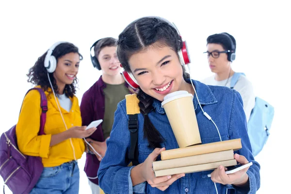 Teen student girl in headphones with coffee to go isolated on white with her friends chatting on background — Stock Photo