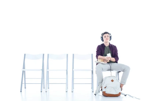 Нудний студент-підліток слухає музику, сидячи на стільці ізольовано на білому — стокове фото