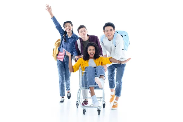 Teen students riding their friend on shopping cart isolated on white — Stock Photo