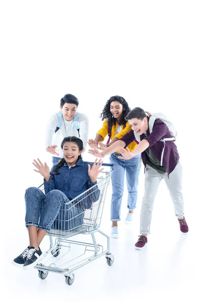 Grupo de estudiantes adolescentes montando a su amigo en el carrito de compras aislado en blanco - foto de stock