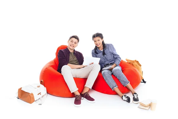 Estudiantes adolescentes que estudian juntos mientras están sentados en bolsas de frijoles aislados en blanco - foto de stock