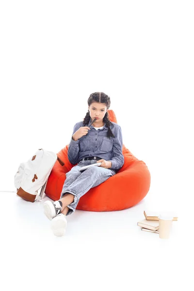 Bored teenage student girl studying while sitting on bean bag isolated on white — Stock Photo