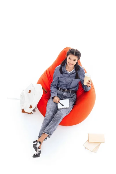 High angle view of teenage student girl studying while sitting on bean bag isolated on white — Stock Photo