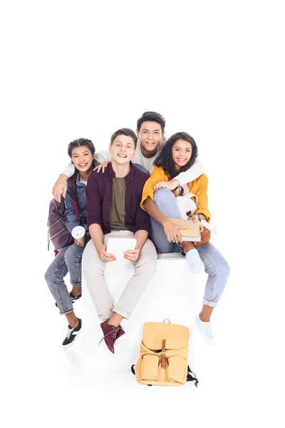 Group of happy teen students sitting on white cube isolated on white — Stock Photo