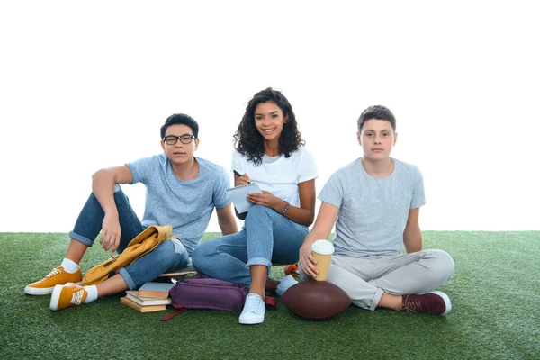 Groupe d'étudiants multiethniques étudiant tout en étant assis sur l'herbe isolé sur blanc — Photo de stock