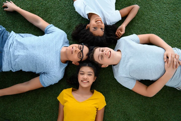 Вид сверху на группу подростков, отдыхающих на зеленой траве — стоковое фото