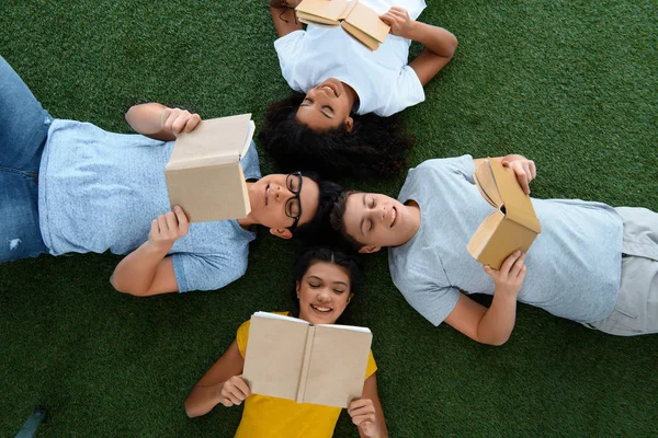 Blick von oben auf eine Gruppe von Teenagern, die Bücher auf grünem Gras lesen — Stockfoto