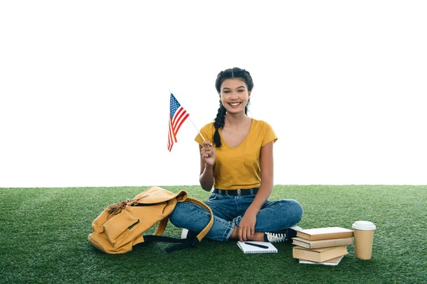Adolescente estudiante chica con usa bandera sentado en hierba aislado en blanco - foto de stock