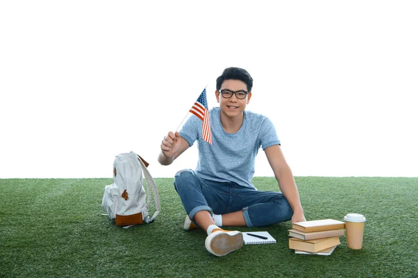 Adolescente asiático estudiante chico con usa bandera sentado en hierba aislado en blanco - foto de stock